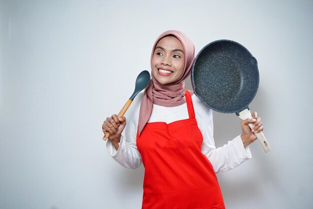 Joven ama de casa asiática con delantal de cocina cocinando y sosteniendo una sartén y una espátula