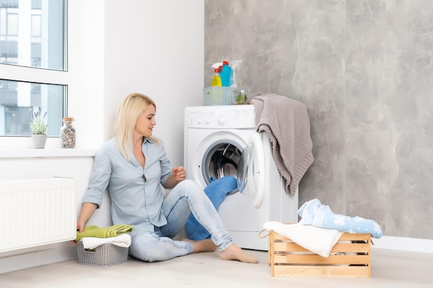 Una joven ama de casa con lavadora y ropa. Día de lavado.