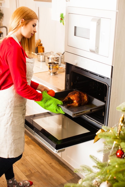 Joven ama de casa sacando pavo asado del horno en una cocina moderna y elegante. cocina navideña en casa