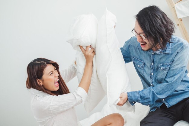 Foto joven amante de la pareja asiática jugando pelea de almohadas en la cama blanca amante de la pareja asiática para el concepto de san valentín