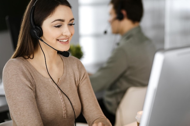 Foto una joven amigable con auriculares está hablando con el cliente de una empresa, mientras está sentada en el escritorio de una oficina moderna junto con su colega. operadores de call center en el trabajo.