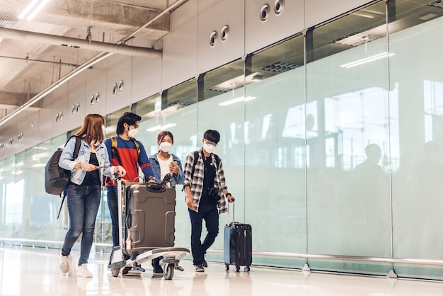 Joven amigo feliz viajero en cuarentena por coronavirus con máscara quirúrgica protección facial con pasaporte y boleto antes de un largo viaje de vacaciones en el aeropuerto de la terminal internacional