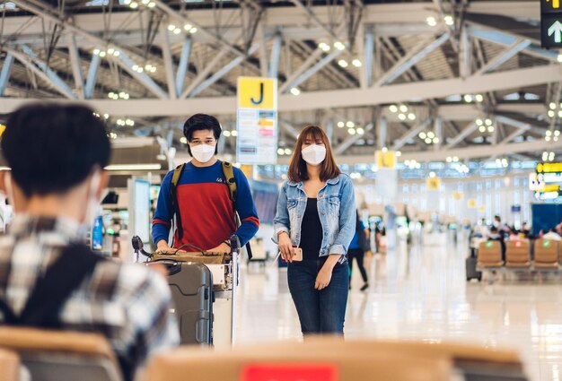 Foto joven amigo feliz viajero en cuarentena por coronavirus con máscara quirúrgica protección facial con pasaporte y boleto antes de un largo viaje de vacaciones en el aeropuerto de la terminal internacional