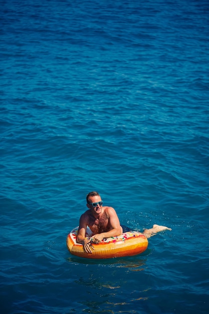 Joven en un anillo inflable en el mar descansando y nadando en un día soleado