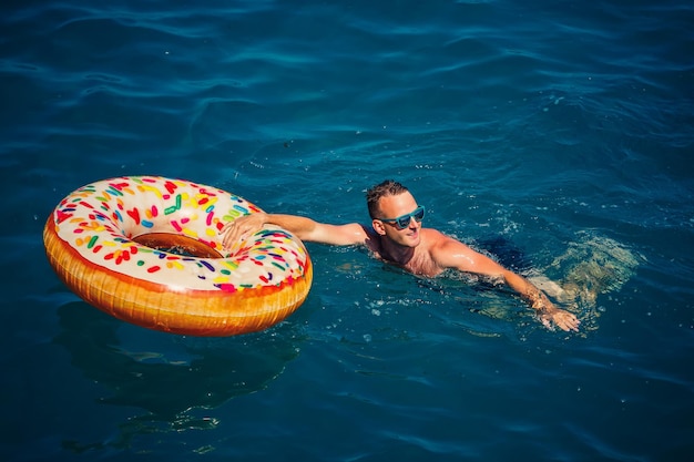 Joven en un anillo inflable en el mar descansando y nadando en un día soleado