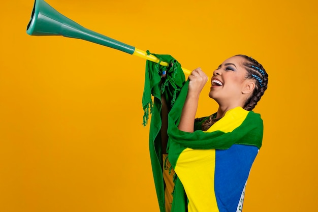 Joven animadora brasileña con una vuvuzela sobre fondo amarillo celebrando