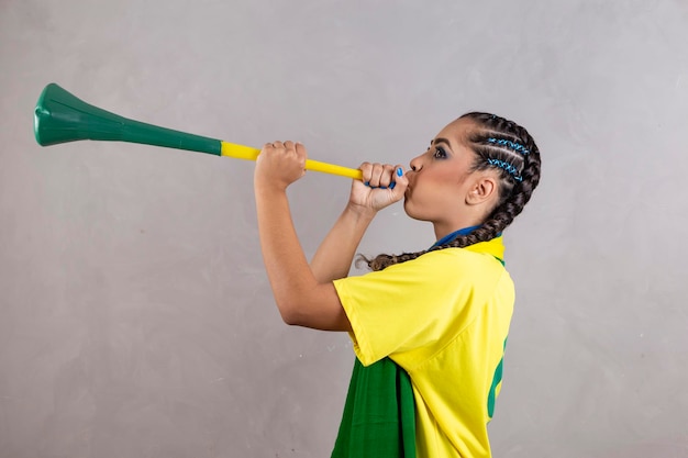 Joven animadora brasileña con una vuvuzela sobre fondo gris celebrando