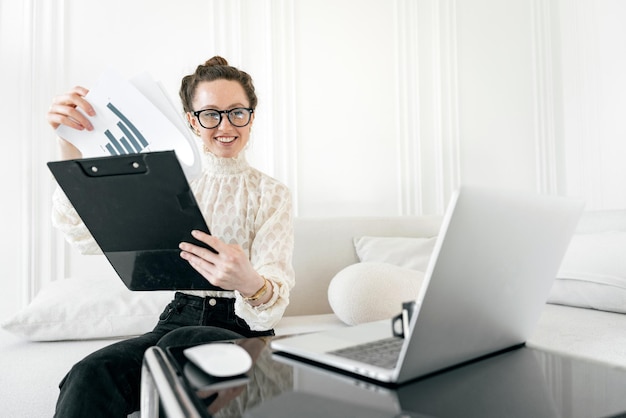 Una joven con anteojos es una empresaria que usa una computadora para un informe en línea en la oficina