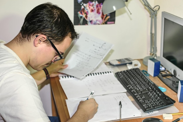 Joven con anteojos estudiando concentrado en su escritorio con su computadora