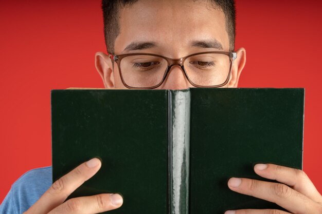 Joven con anteojos leyendo un libro de tapa dura sosteniéndolo frente a su cara