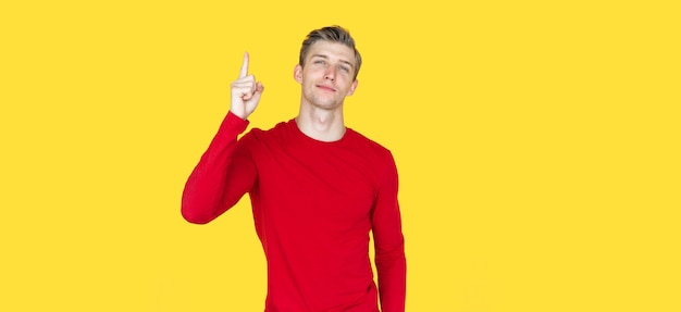 Joven de apariencia europea sobre fondo amarillo. señala con el dedo índice al espacio en blanco de arriba