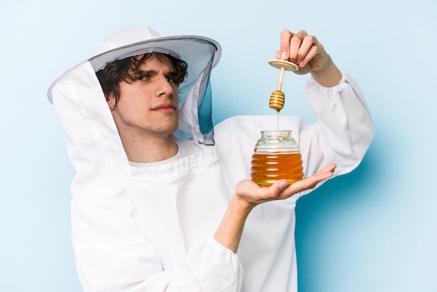 Joven apicultor caucásico sosteniendo miel aislada de fondo azul