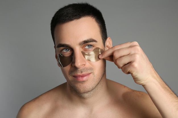 Joven aplicando bajo parches en los ojos sobre fondo gris