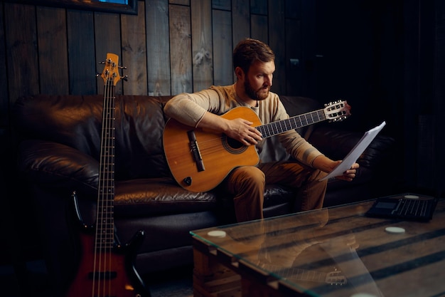 Joven aprendiendo a tocar la guitarra en casa leyendo notas musicales. Lección online, educación a distancia