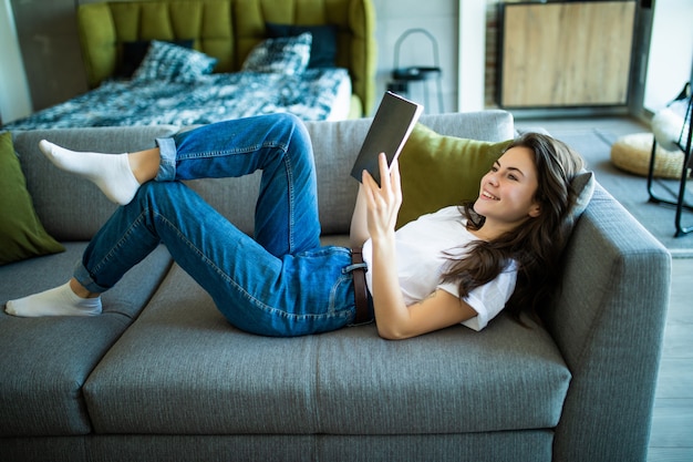 Joven apuesta leyendo un libro mientras está acostado en un sofá en la sala de estar