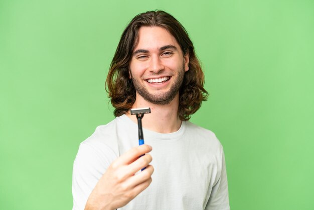 Un joven apuesto afeitándose la barba sobre un fondo aislado con expresión feliz