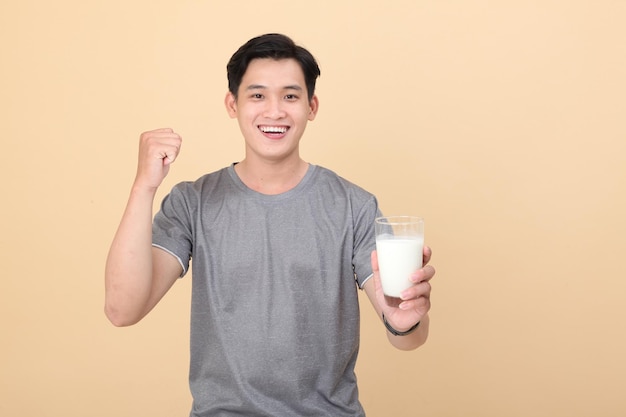 Un joven apuesto y alegre, deportivo asiático, sostiene un vaso de leche fresca aislado en el fondo