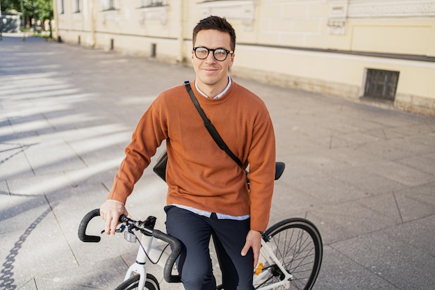 Un joven apuesto con anteojos y una bicicleta al fondo de una pared en la ciudad