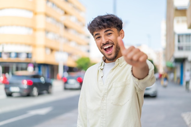 Joven apuesto árabe al aire libre con los pulgares hacia arriba porque algo bueno ha sucedido