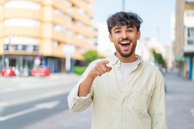 Joven apuesto árabe al aire libre sorprendido y apuntando al frente