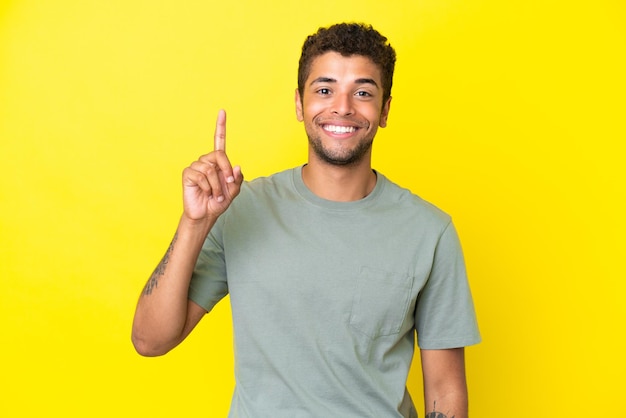 Joven apuesto brasileño aislado de fondo amarillo señalando una gran idea