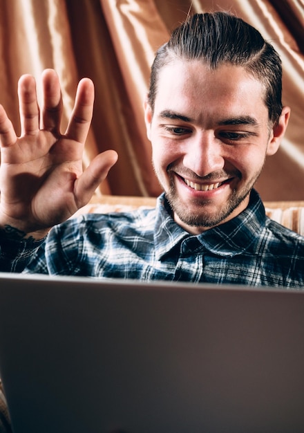 un joven apuesto con una camisa azul se comunica a través de un enlace de video en una laptop plateada