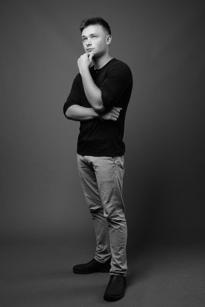 joven apuesto con camisa negra contra la pared gris. en blanco y negro