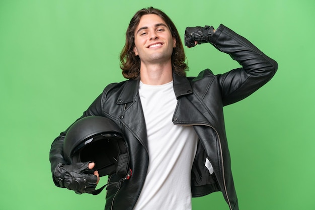 Un joven apuesto con un casco de motocicleta aislado en un fondo de croma verde haciendo un gesto fuerte