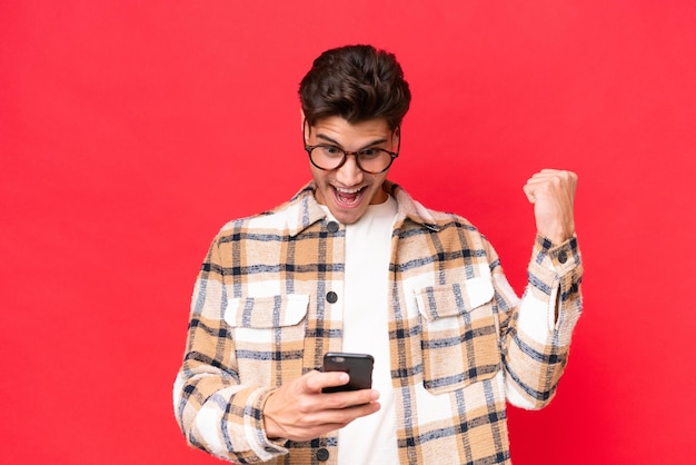 Joven apuesto caucásico aislado de fondo rojo sorprendido y enviando un mensaje