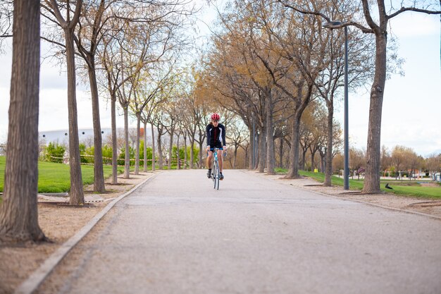 Joven apuesto ciclista masculino en ropa deportiva y casco protector bicicleta ciclismo en carretera en el parque