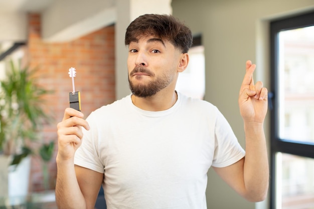 Foto joven apuesto cruzando los dedos y esperando buena suerte nuevo concepto clave de hogar