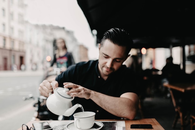 un joven apuesto desayuna y bebe té y café por la mañana en la terraza de un restaurante