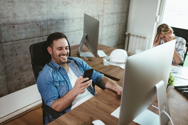 Joven apuesto y exitoso empresario independiente divirtiéndose y trabajando en la computadora en la oficina. Está navegando en las redes sociales.