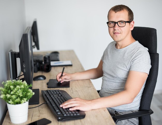 Joven y apuesto fotógrafo masculino editando imágenes con una computadora en una oficina moderna o en casa