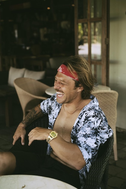 Joven apuesto hippie con un pañuelo rojo, con el torso desnudo en un café de Bali. hombre feliz sonriendo
