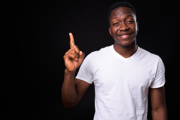 Joven apuesto hombre africano con pelo afro contra la pared negra