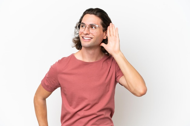 Joven apuesto hombre aislado de fondo blanco escuchando algo poniendo la mano en la oreja