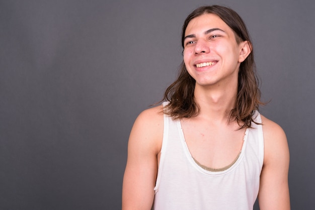 Joven apuesto hombre andrógino con cabello largo contra la pared gris