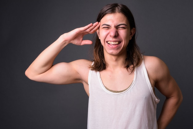 Joven apuesto hombre andrógino con cabello largo contra la pared gris