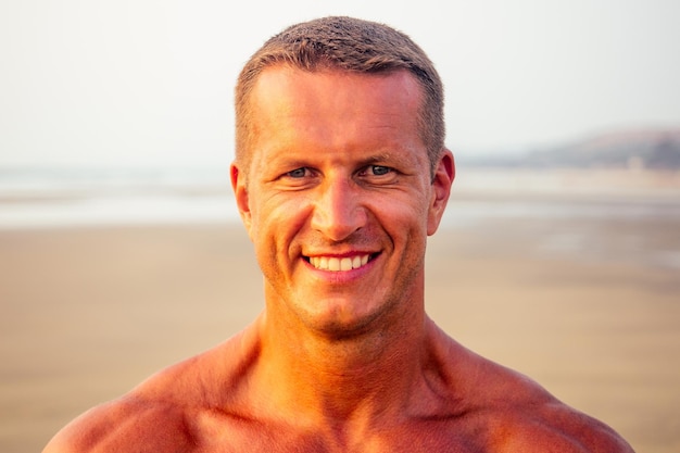 Joven apuesto hombre aplicando crema protector solar en la playa del mar.Modelo masculino sexy atleta culturista posando el cuerpo atlético perfecto, depilación y concepto de depilación shugaring