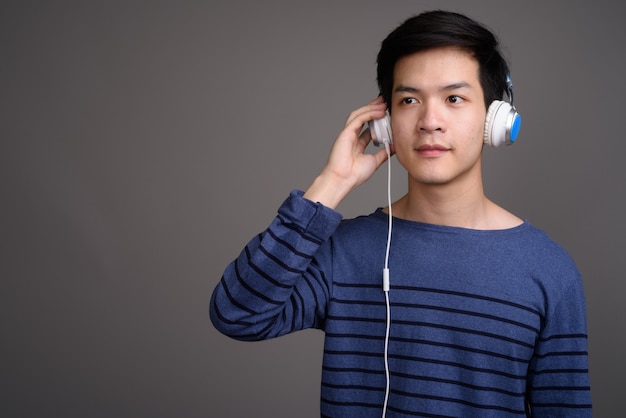 Joven apuesto hombre asiático escuchando música en gris