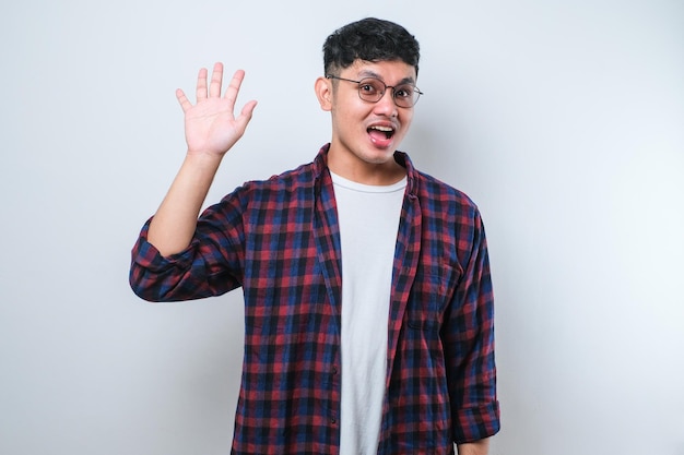 Joven apuesto hombre asiático renunciando a decir hola feliz y sonriente gesto de bienvenida amistoso