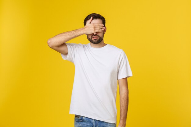 Joven apuesto hombre caucásico aislado en beige cubriendo los ojos con las manos No quiero ver algo