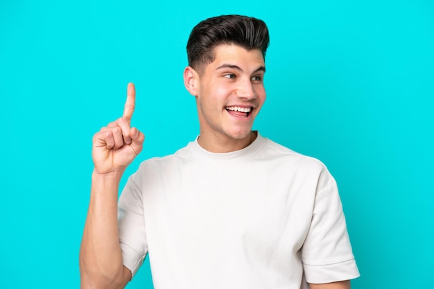 Foto joven apuesto hombre caucásico aislado en un fondo azul con la intención de darse cuenta de la solución mientras levanta un dedo