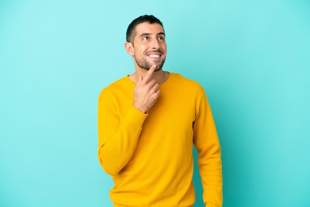 Joven apuesto hombre caucásico aislado de fondo azul mirando hacia arriba mientras sonríe