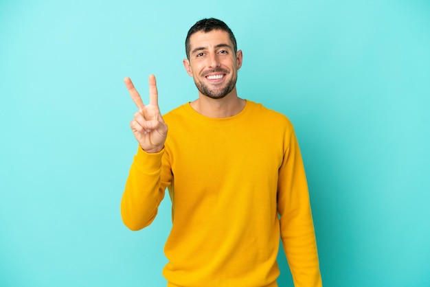 Joven apuesto hombre caucásico aislado de fondo azul sonriendo y mostrando el signo de la victoria