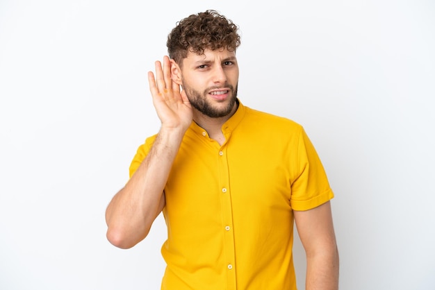 Foto joven apuesto hombre caucásico aislado de fondo blanco escuchando algo poniendo la mano en la oreja