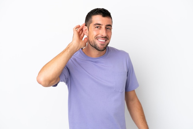 Foto joven apuesto hombre caucásico aislado de fondo blanco escuchando algo poniendo la mano en la oreja