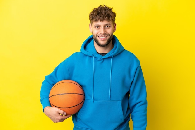 Joven apuesto hombre caucásico aislado sobre fondo amarillo jugando baloncesto