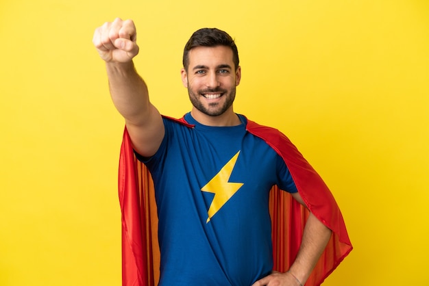 Joven apuesto hombre caucásico aislado sobre fondo amarillo en traje de superhéroe con gesto orgulloso